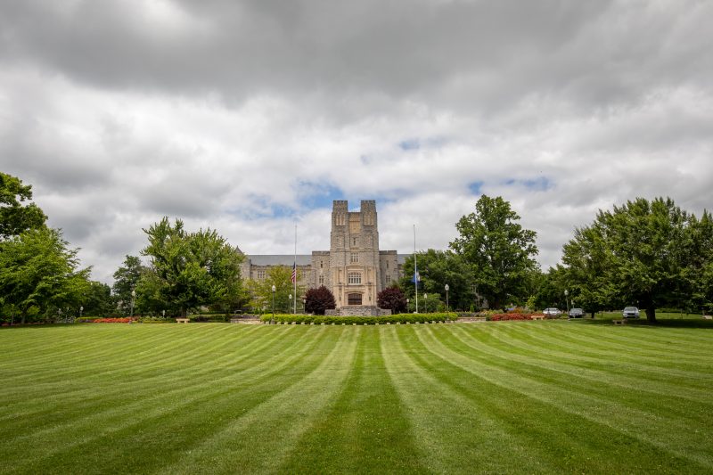 Grey Hokie Stone Burruss Hall on a partially cloudy summer day. The Drillfield grass leading up to the building is freshly mowed with lines leading the eye to the building.