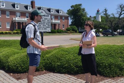 Aaron Whittemore and Anamaria Bukvic face each other in conversation while standing outside a red brick building.