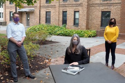 Three people physically distanced in front of a brick building