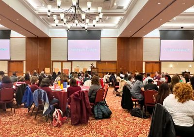 People sitting at tables listening to a speaker. at a conference.