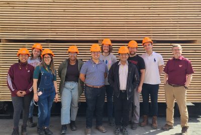 A group of students wearing hard hats stand in front of a large pallet of wood.