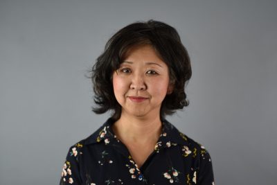 Headshot of Aki Ishida in a black floral blouse.