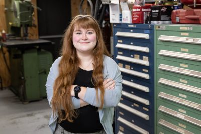 ECE Alumna Megan Bennett stands with her arms crossed in front of toolboxes.