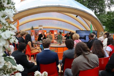 Presenters speak to a seated crowd in a garden observatory.
