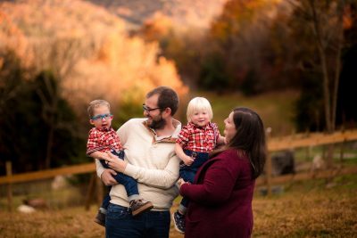 Family of four laughing with fall leaves in the backgroud.