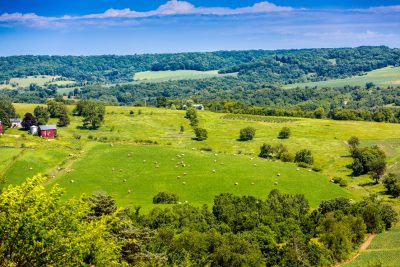 Rural image of midwestern farmland of rolling hills, green meadows, and red barn off in the distance.  