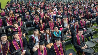 A group of students in black graduation regalia sitting in chairs